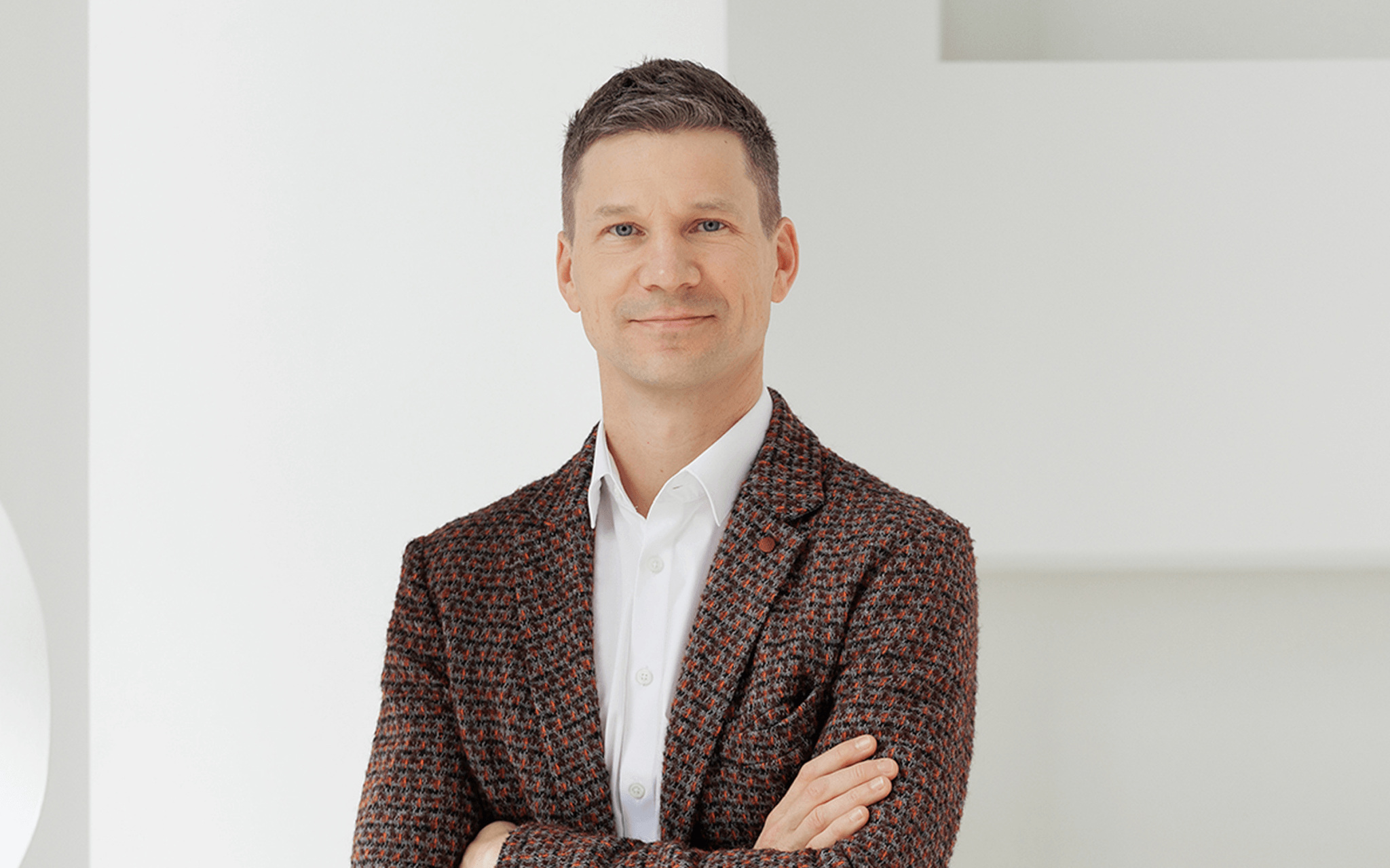 Professionelles Porträt eines Mannes in rotem Tweed-Blazer und weißem Hemd vor neutralem Hintergrund.